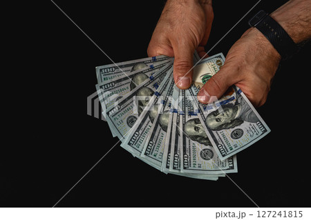Hands displaying multiple hundred dollar bills in low light 127241815