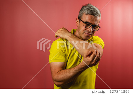 Man examining his arm for discomfort against a colored backdrop 127241893