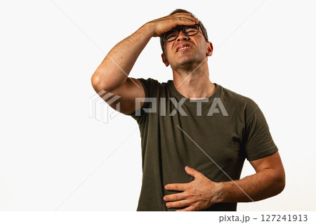 Man holds his stomach in discomfort while standing indoors 127241913