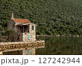 An old stone house stands still by the water, wrapped in the silence of green hills. 127242944