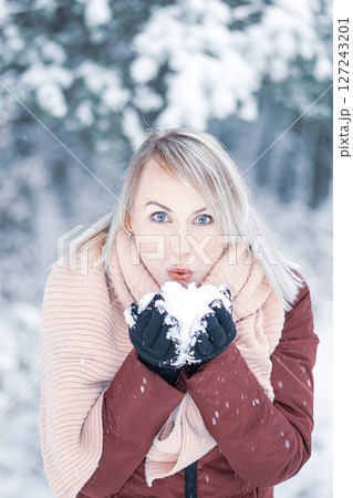 Woman blowing snow in her hands during winter time in forest background 127243201