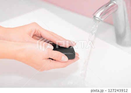 Woman washing hands with black soap over sink 127243912