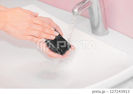 Woman washing hands with black soap over sink 127243913