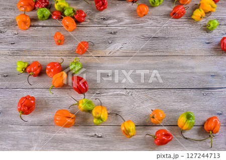Fresh habanero peppers in various colors are scattered on weathered wooden table, showcasing their vibrant appearance. 127244713