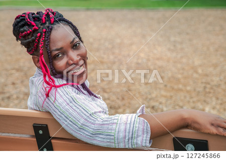 Relaxed African American Woman with Pink Braids Sitting on Park Bench Outdoors 127245866