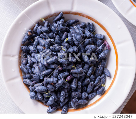 Large blue honeysuckle berries in a plate on the table in June Large blue honeysuckle berries in a plate on the table in June 127248047