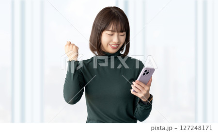 スマートフォンを見てガッツポーズをする若い女性・ビジネスウーマン スマートフォンを見てガッツポーズをする若い女性・ビジネスウーマン 127248171
