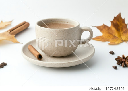 Spicy cappuccino cup or spice latte with art foam, cinnamon stick and anise stars. Autumn leaves. Warm Coffee, white surface. Cozy fall drink on a table. Inviting atmosphere. Mug of warming drink 127248561