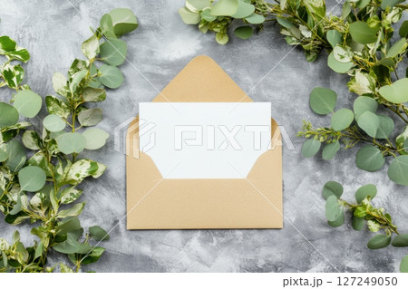 Paper envelope with paper letter peeks open and eucalyptus branch on grey background, close up. Mockup for design. White blank card, formal script for wedding or event invitations. Mock up, template 127249050