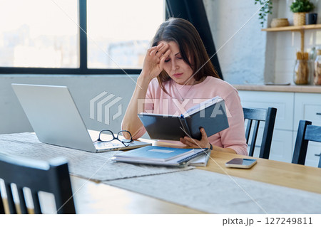 Middle aged sad stressed woman sitting at home office at table with computer Middle aged sad stressed woman sitting at home office at table with computer 127249811