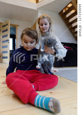 A Young Girl with a Curious Cat in a Cozy Home Setting, Showcasing Playful Moments and Warm Family Bonds on a Beautiful Wooden Floor A Young Girl with a Curious Cat in a Cozy Home Setting, Showcasing Playful Moments and Warm Family Bonds on a Beautiful Wooden Floor 127250094