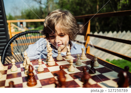 Schoolboy playing board game - wooden chess. Little boy child moves a pawn piece Schoolboy playing board game - wooden chess. Little boy child moves a pawn piece 127250789