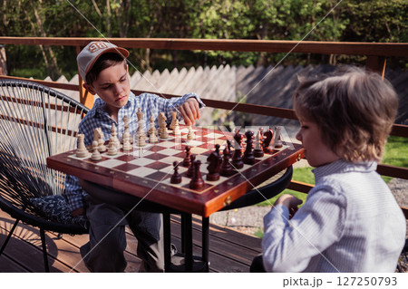 Little boys friends playing board game - chess. Children learning to move pieces Little boys friends playing board game - chess. Children learning to move pieces 127250793