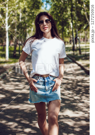 Happy Young Woman In White T-Shirt And Denim Skirt Walking In Park 127250916