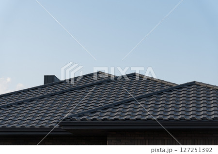 Dark tiled roofs rise against a pale blue sky, showcasing modern architecture in a peaceful suburban setting during late afternoon Dark tiled roofs rise against a pale blue sky, showcasing modern architecture in a peaceful suburban setting during late afternoon 127251392