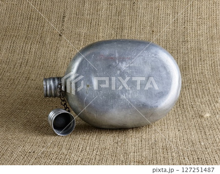 Old soldier's aluminum flask on burlap. A thermos for water. An empty flask with an unscrewed cap. 127251487