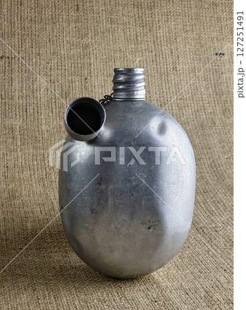 Old soldier's aluminum canteen with lid on chain on burlap. Thermos for water. Empty canteen with an unscrewed stopper. Old soldier's aluminum canteen with lid on chain on burlap. Thermos for water. Empty canteen with an unscrewed stopper. 127251491