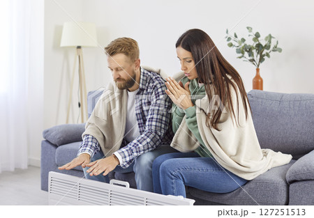 Freezing couple wrapped in plaids sitting near electric heater trying to warm up during cold winter. Freezing couple wrapped in plaids sitting near electric heater trying to warm up during cold winter. 127251513