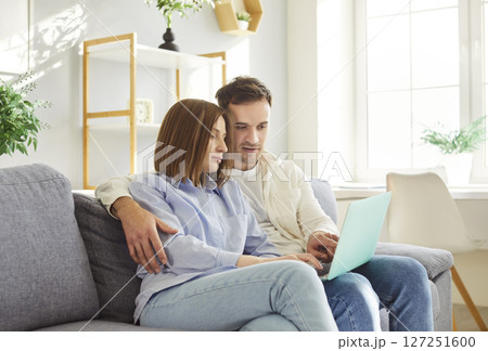 Young family, loving spouses sitting close on sofa, relaxing together at home using laptop computer Young family, loving spouses sitting close on sofa, relaxing together at home using laptop computer 127251600