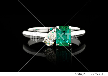 silver or gold ring with emerald stone and diamonds on black background 127253315