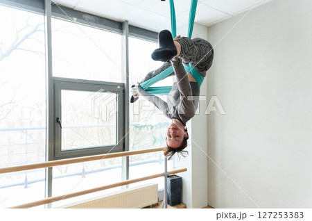 Athletic woman performing an inverted pose on teal aerial silks. Athletic woman performing an inverted pose on teal aerial silks. 127253383