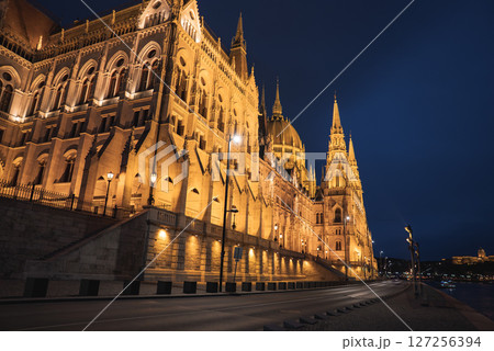 The Hungarian Parliament Building in Budapest glows at night with warm lighting, showcasing its neo Gothic architecture, spires, and domes by the Danube River. 127256394