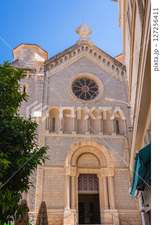 The Romanesque cathedral in Cannes, France, features a rose window, arched doorways, and detailed stonework, framed by nearby buildings and a tree. The Romanesque cathedral in Cannes, France, features a rose window, arched doorways, and detailed stonework, framed by nearby buildings and a tree. 127256411
