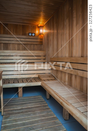 Wooden sauna interior with tiered benches, warm ambient lighting, a wooden mat on the floor, and functional dials on the back wall. 127256423