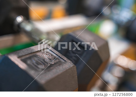 A 10 kg hexagonal dumbbell with embossed weight detail, set against a blurred background of gym equipment in a luxury fitness center. 127256800