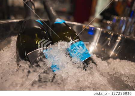 Two dark glass bottles with blue labels rest in a metal ice bucket filled with crushed ice. The blurred background suggests a luxurious setting. 127256936