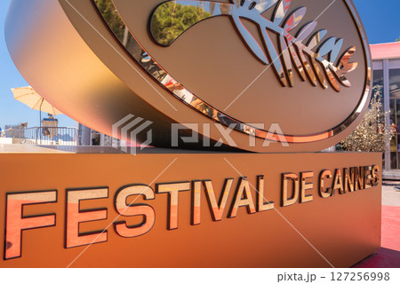 Golden Festival de Cannes sign with logo, reflecting trees and outdoor seating. Red carpet in the background suggests a sunny day in Cannes, France. Golden Festival de Cannes sign with logo, reflecting trees and outdoor seating. Red carpet in the background suggests a sunny day in Cannes, France. 127256998