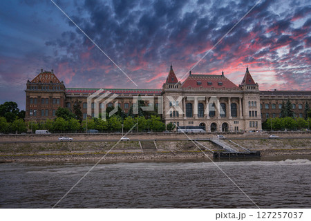 The ornate facade of the Budapest University of Technology and Economics with red tiled roofs and towers, set against a vibrant pink and purple sunset sky. The ornate facade of the Budapest University of Technology and Economics with red tiled roofs and towers, set against a vibrant pink and purple sunset sky. 127257037
