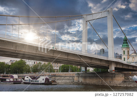 The Elisabeth Bridge in Budapest, Hungary, with its white suspension design, boats along the riverbank, and a green domed church in the background. The Elisabeth Bridge in Budapest, Hungary, with its white suspension design, boats along the riverbank, and a green domed church in the background. 127257082