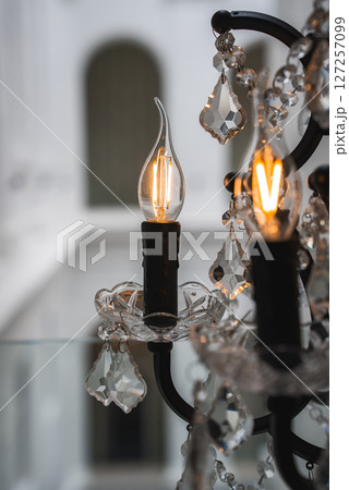 Elegant chandelier with intricate crystal details and glowing candle style bulbs, set against a blurred arched architectural background. Elegant chandelier with intricate crystal details and glowing candle style bulbs, set against a blurred arched architectural background. 127257099