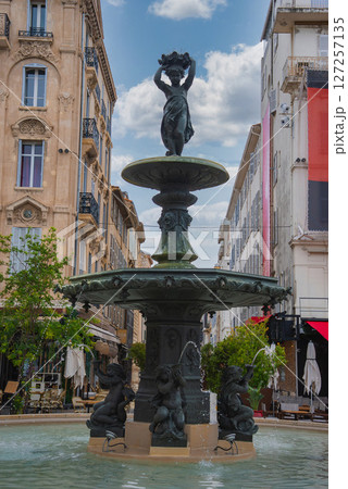 A public square in Cannes, France, featuring a fountain with a statue of a woman holding a wreath, cherub sculptures, and ornate European buildings. A public square in Cannes, France, featuring a fountain with a statue of a woman holding a wreath, cherub sculptures, and ornate European buildings. 127257135