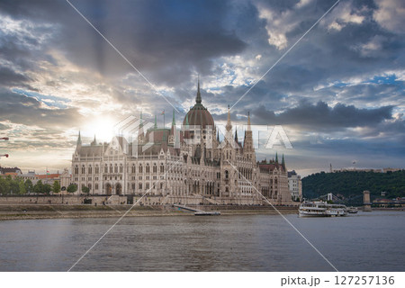The neo Gothic Hungarian Parliament Building stands by the Danube River in Budapest, with a boat on the water and hills in the background. 127257136