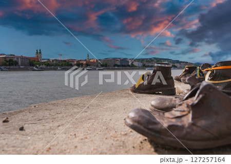 The Shoes on the Danube Bank memorial in Budapest, Hungary, with bronze shoes by the river, historic landmarks, and a colorful sunset sky. The Shoes on the Danube Bank memorial in Budapest, Hungary, with bronze shoes by the river, historic landmarks, and a colorful sunset sky. 127257164