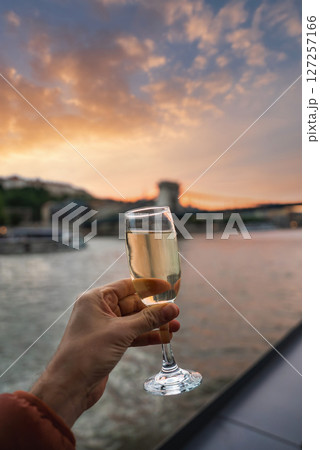 A glass of champagne is held in the foreground, with Budapest's Szechenyi Chain Bridge and the Danube River illuminated by a warm sunset glow. A glass of champagne is held in the foreground, with Budapest's Szechenyi Chain Bridge and the Danube River illuminated by a warm sunset glow. 127257166