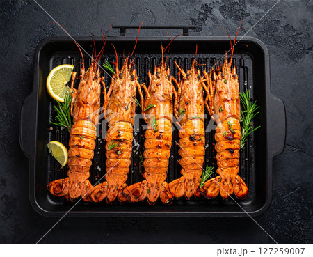 AI generated top view of fresh mantis shrimp grilled over charcoal, perfectly cooked with smoky aroma and succulent meat. Seasoned with salt and black pepper, garnished with rosemary and lemon slices. 127259007