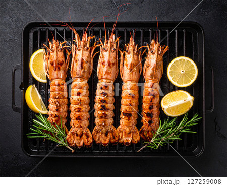 AI generated top view of fresh mantis shrimp grilled over charcoal, perfectly cooked with smoky aroma and succulent meat. Seasoned with salt and black pepper, garnished with rosemary and lemon slices. 127259008