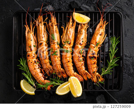 AI generated top view of fresh mantis shrimp grilled over charcoal, perfectly cooked with smoky aroma and succulent meat. Seasoned with salt and black pepper, garnished with rosemary and lemon slices. 127259009
