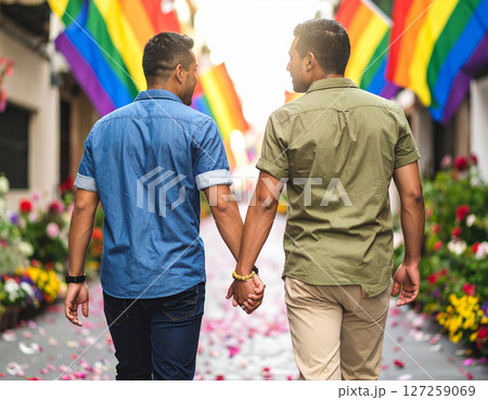 AI generated image of two men in love holding hands walking down a street lined with rainbow pride flags and colorful flowers representing LGBTQ romance diversity and acceptance 127259069