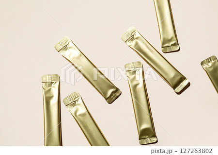 Several Golden Stick Packaging Sachets on Light Background. Unbranded Foil Pouch Mockup for Product Presentation. 127263802