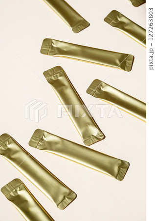 Golden Metallic Stick Packaging on Light Background. Small Packets for Food, Medicine or Cosmetic Product. Golden Metallic Stick Packaging on Light Background. Small Packets for Food, Medicine or Cosmetic Product. 127263803