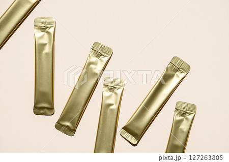 Multiple Golden Foil Stick Packs and Sachets on Beige Background. Mockup for a Quick Food Product, Skincare or Medicine. Multiple Golden Foil Stick Packs and Sachets on Beige Background. Mockup for a Quick Food Product, Skincare or Medicine. 127263805