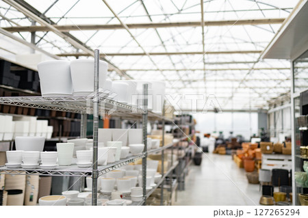 A shop selling a variety of white flower pots on display, arranged on metal shelving under a bright glass ceiling, ready for plants. 127265294