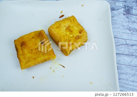 Two golden-fried tofu squares sit on a white rectangular plate against a light, textured background. 127266513