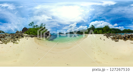 A serene beach with rocky formations and soft sand, leading into clear, calm waters with lush greenery in the background. Port Glaud Lagoon. Seychelles. VR 360. A serene beach with rocky formations and soft sand, leading into clear, calm waters with lush greenery in the background. Port Glaud Lagoon. Seychelles. VR 360. 127267510