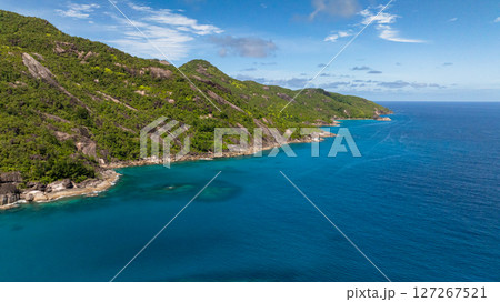 Green mountainous coastline descending into crystal clear turquoise waters under a blue sky. Seychelles, Mahe. Victoria. Green mountainous coastline descending into crystal clear turquoise waters under a blue sky. Seychelles, Mahe. Victoria. 127267521