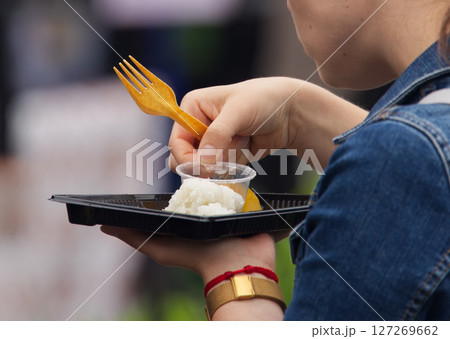 Close-Up of Person Eating Meal from Plastic Container with Utensil Outdoors 127269662